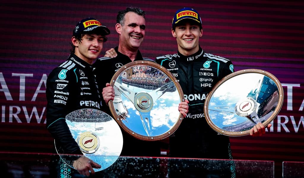 Andrea Kimi Antonelli, Toto Wolff, and George Russell holding Formula 1 podium trophy plates after a race.