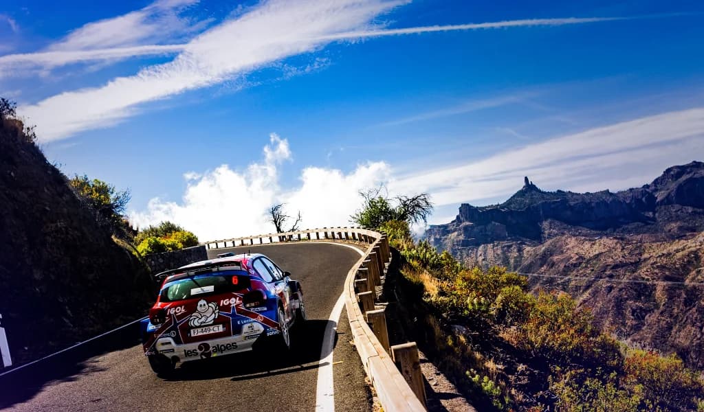 Rally car driving along a winding mountain road in a scenic landscape.