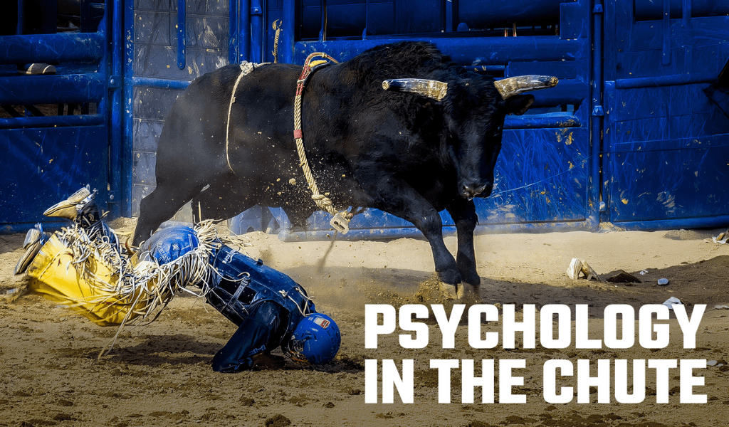 Fallen bull rider in blue helmet crouching near a black bull by the chute gate with text Psychology in the Chute.
