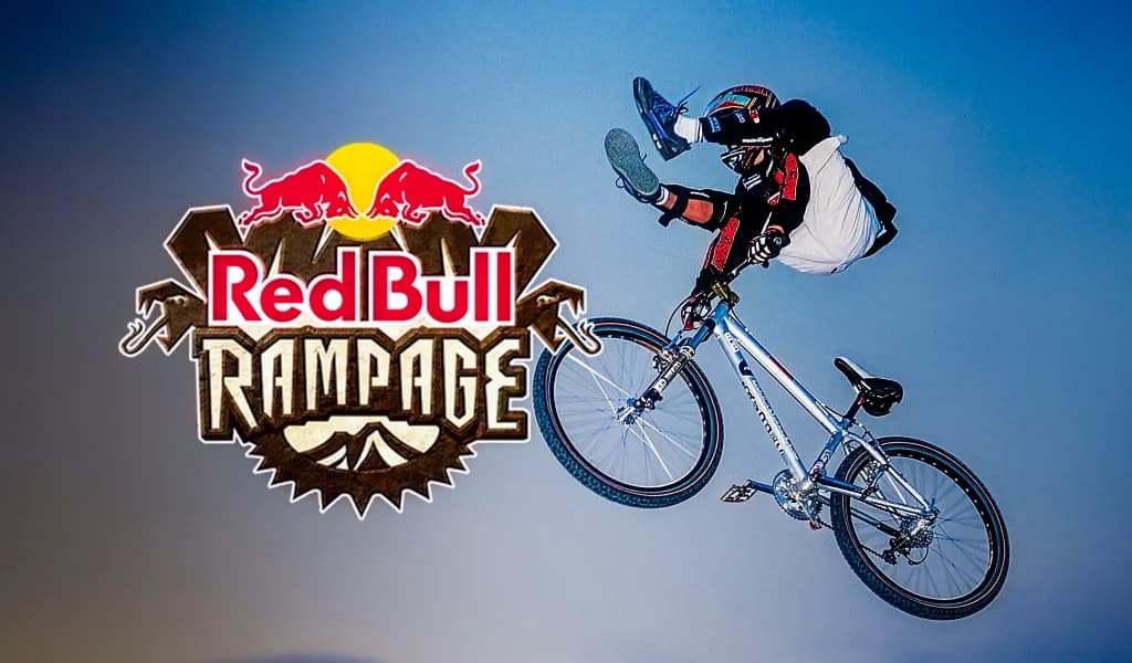 Kyle Strait performing a no-footer trick in the air alongside the Red Bull Rampage logo against a blue sky.