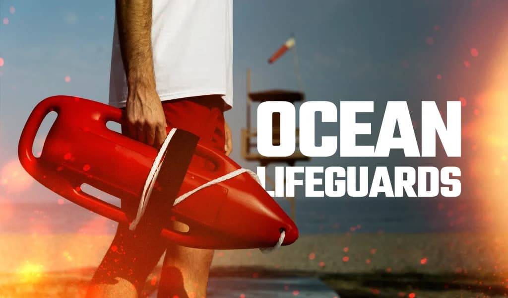 Person holding a red rescue buoy near the shoreline with an ocean lifeguard tower in the background.