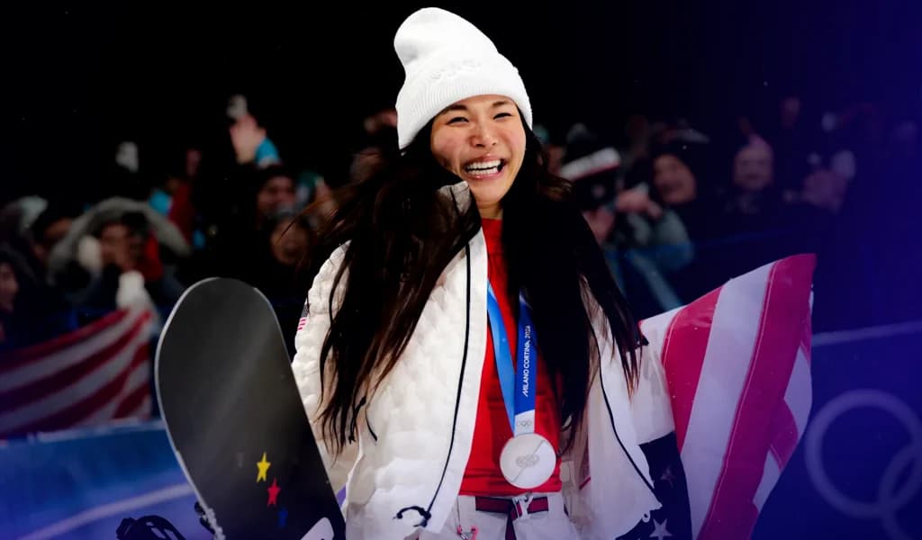 Chloe Kim smiling with her silver medal while holding a snowboard and the U.S. flag.