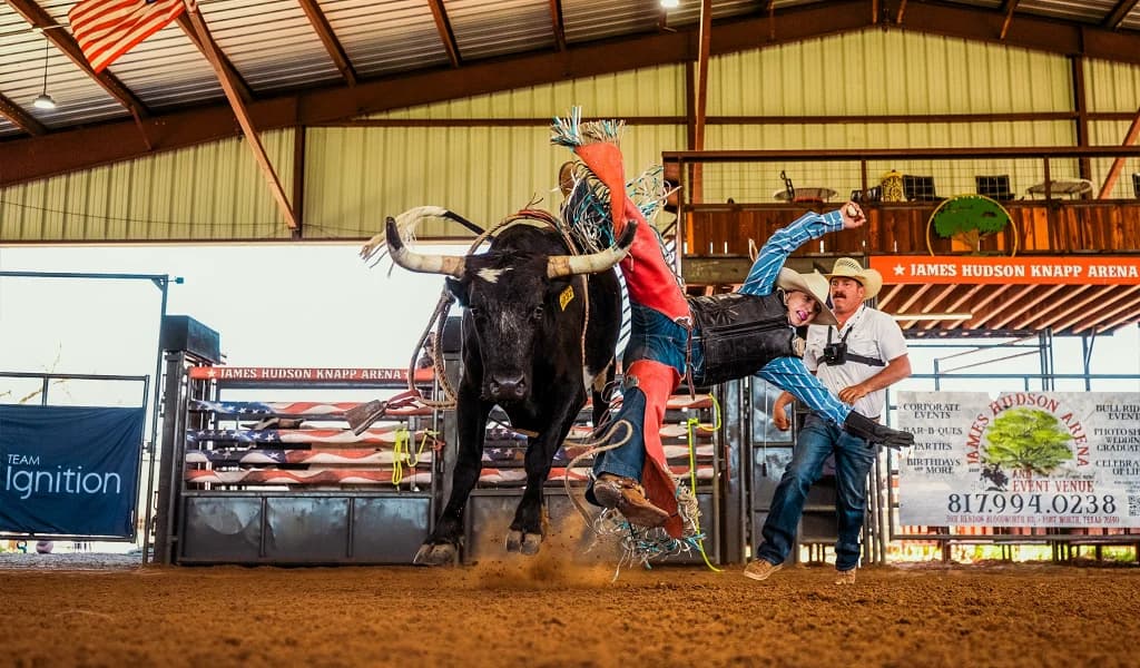 Jorden Halvorsen being thrown from a bull at James Hudson Knapp Arena with a Team Ignition banner visible in the background.