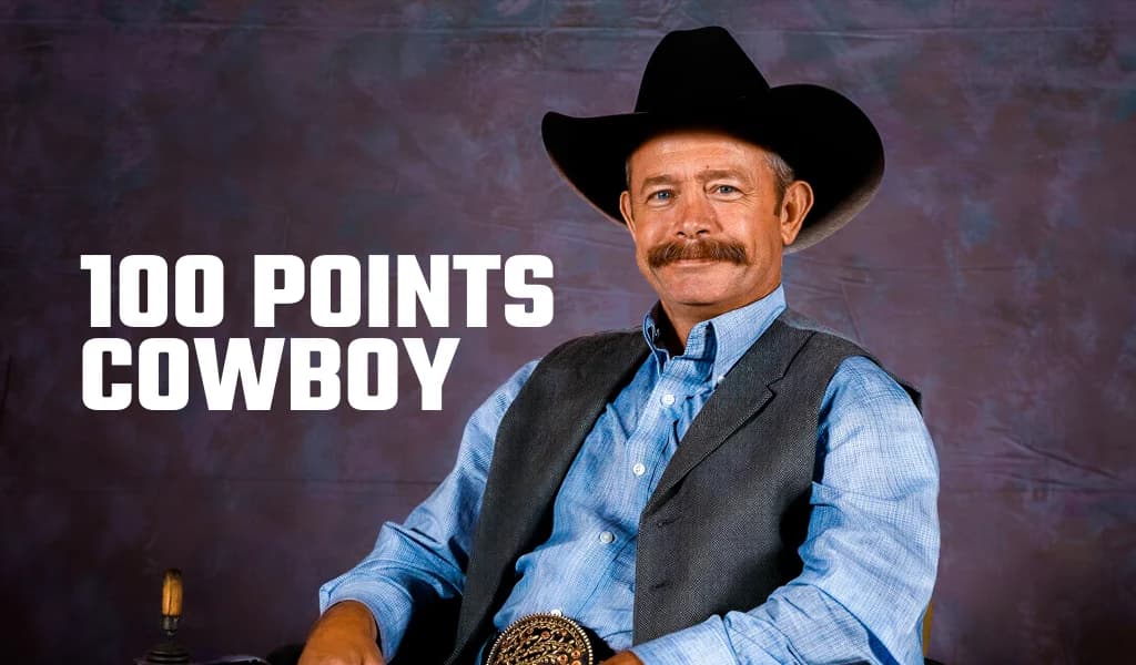 Wade Lesley in black cowboy hat, vest and large belt buckle seated against a grey backdrop with text 100 Points Cowboy.