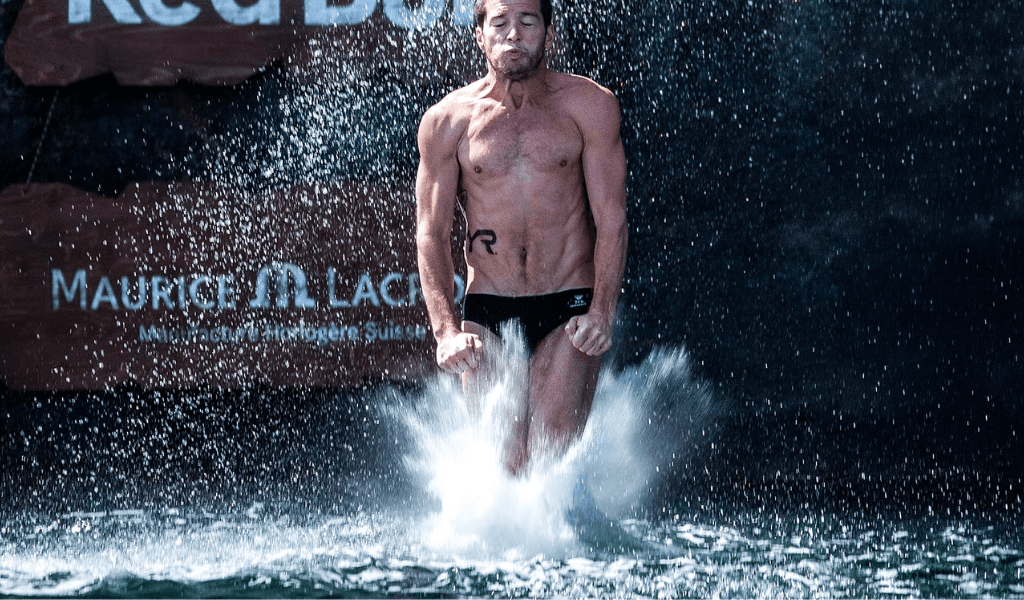 Male diver entering the water feet first at a Red Bull cliff diving event with water spraying around him.