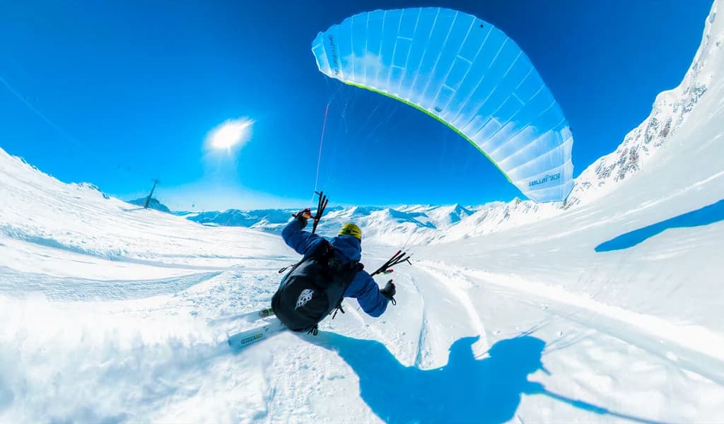A fisheye view of a skier carving down a snowy slope with a blue speed wing overhead.