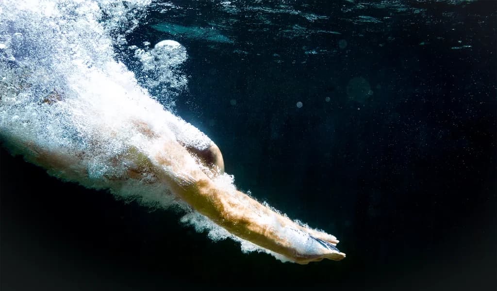 An underwater view of a diver entering the water in a streamlined, arms-first position.