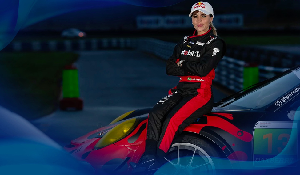 Leticia Bufoni in a racing suit and cap, sitting on a race car, arms crossed and smiling, with a racetrack in the background