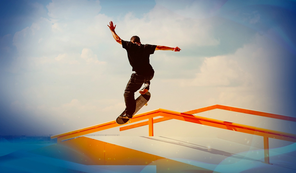 Skateboarder mid-grind on an orange rail with one arm raised, set against a bright background.