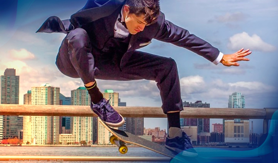 William Spencer skateboarding in a suit while performing a trick, city skyline in the background.