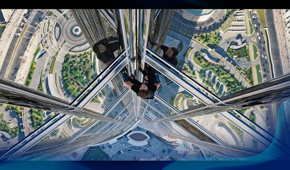 Aerial view of a man scaling a tall skyscraper, with a cityscape seen from above, performing a daring stunt.