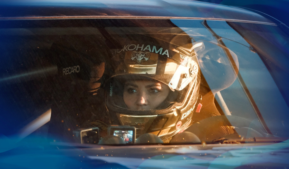 Close-up of Leticia Bufoni wearing a Yokohama-branded helmet inside a race car, her intense focus visible through the windshield