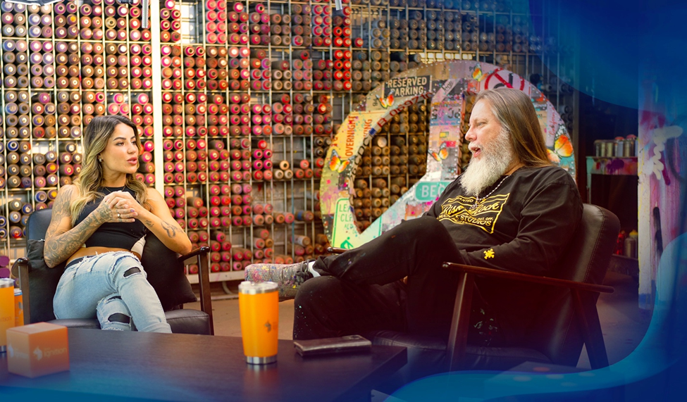 Graffiti artist Risk and Leticia Bufoni chat in a graffiti-covered space surrounded by spray paint cans.