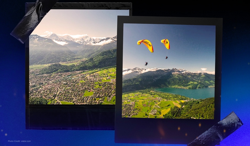 A scenic view of Interlaken, Switzerland, showing a valley surrounded by mountains, and two paragliders soaring above a green lake.