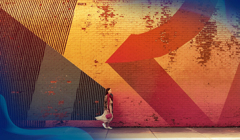 Large geometric mural on a brick wall with a woman walking past.